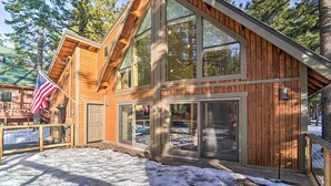Une cabane en bois dotée de grandes fenêtres et d’une terrasse.