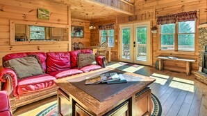 Ein gemütliches Blockhaus-Interieur mit einem roten Ledersofa, einem Holzespeisetisch und einem Kamin aus Naturstein.