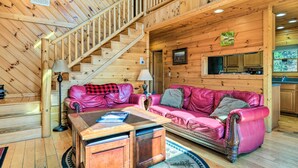Ein Holzinnenraum mit einer Treppe, einem pinken Ledersofa, einem Holztisch und einer Küchenzeile.