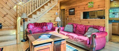 A wooden interior with a staircase, a pink leather sofa, a wooden coffee table, and a kitchen area.