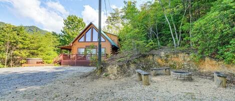 A cabin with a wooden exterior, a deck, and a gravel driveway.