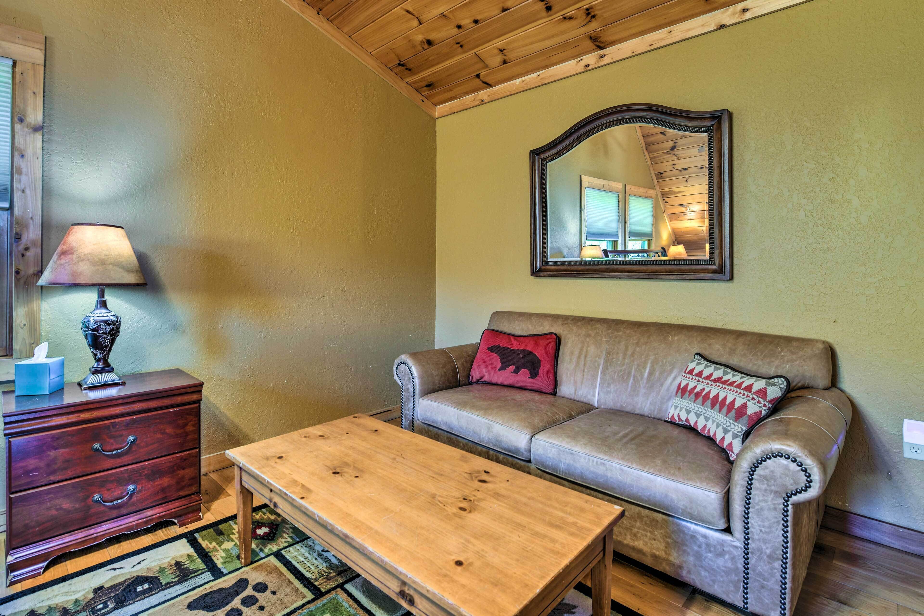 A cozy living room with a wooden coffee table, a leather sofa with decorative pillows, a wooden dresser, and a mirror on the wall.