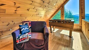 Ein gemütliches Zimmer mit Holzbalkendecke, einem violetten Sofa mit Decke und einem Kicker.