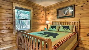 Ein Schlafzimmer einer Holzhütte mit einem Bett, einem Fenster und einem gerahmten Bild an der Wand.