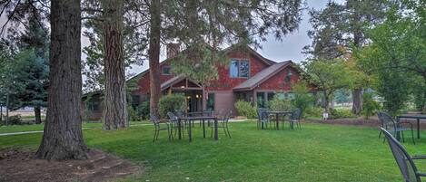 A lodge with a red exterior, outdoor seating area, and large trees.