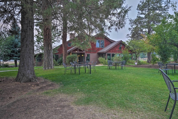 A lodge with a red exterior, outdoor seating area, and large trees.