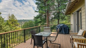 A wooden deck with a table and chairs, a barbecue grill, and a view of trees and hills. - Resort-style Klamath Falls Home, Golf Course View! (Klamath Falls)