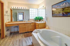 Une salle de bain spacieuse avec une grande baignoire, des meubles en bois, un meuble-lavabo avec un miroir et une grande fenêtre qui laisse entrer la lumière naturelle.