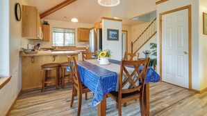 A dining area with a wooden table and chairs, a kitchen in the background, and a staircase leading to another level. - Resort-style Klamath Falls Home, Golf Course View! (Klamath Falls)