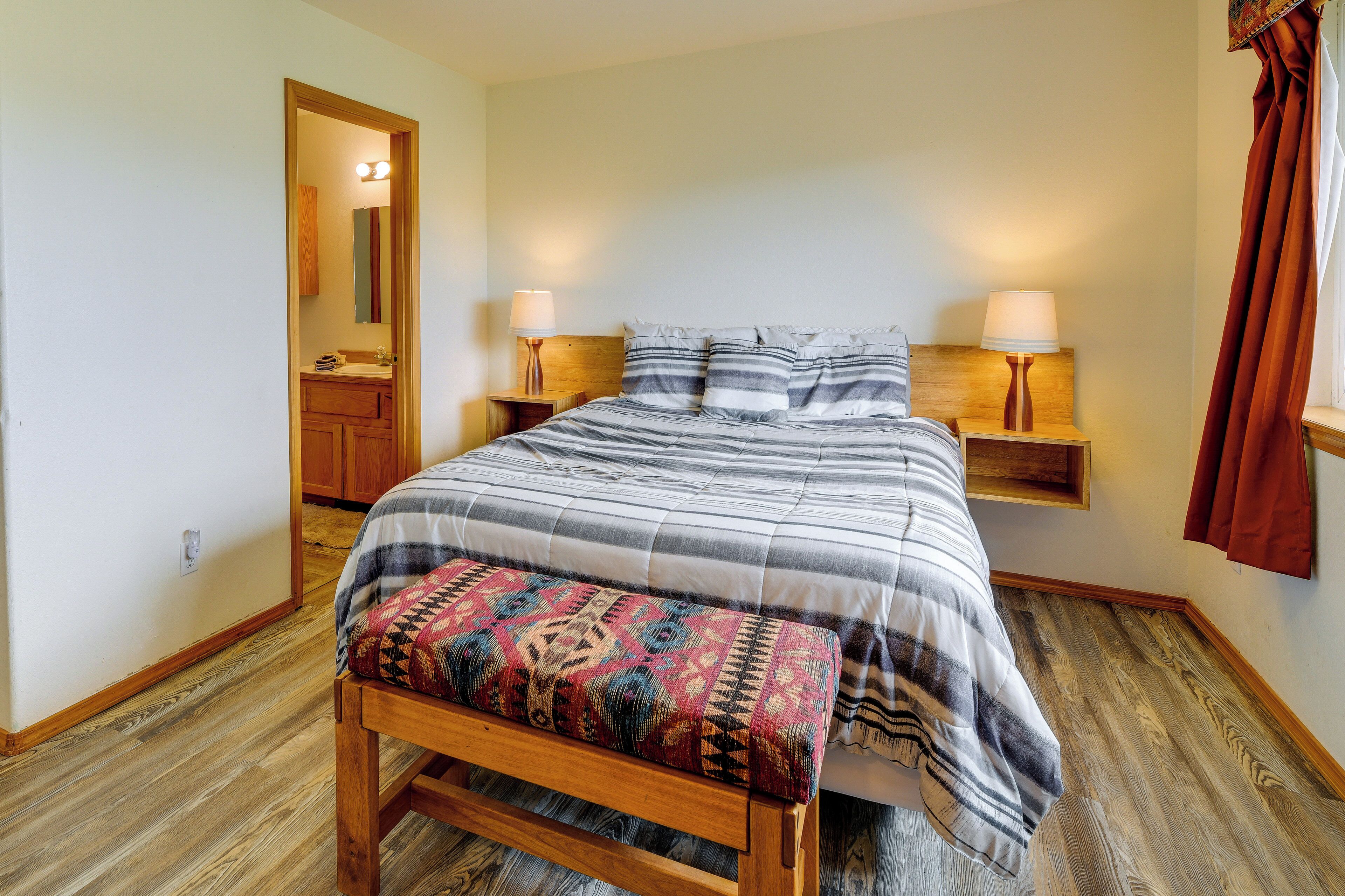 A bedroom with a wooden bench, a bed with striped bedding, two bedside lamps, and a wooden nightstand.