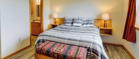 A bedroom with a wooden bench, a bed with striped bedding, two bedside lamps, and a wooden nightstand.