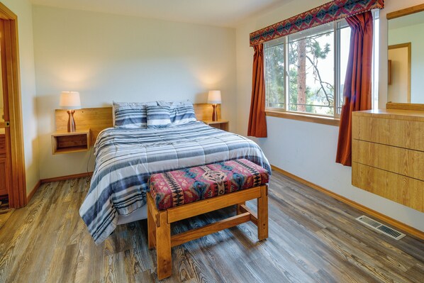 A bedroom with a wooden bed, two bedside tables with lamps, a bench, a window with curtains, and a wooden dresser. - Resort-style Klamath Falls Home, Golf Course View! (Klamath Falls)