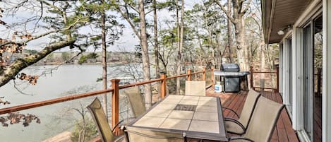 A wooden deck with a table and chairs overlooking a lake, surrounded by trees.