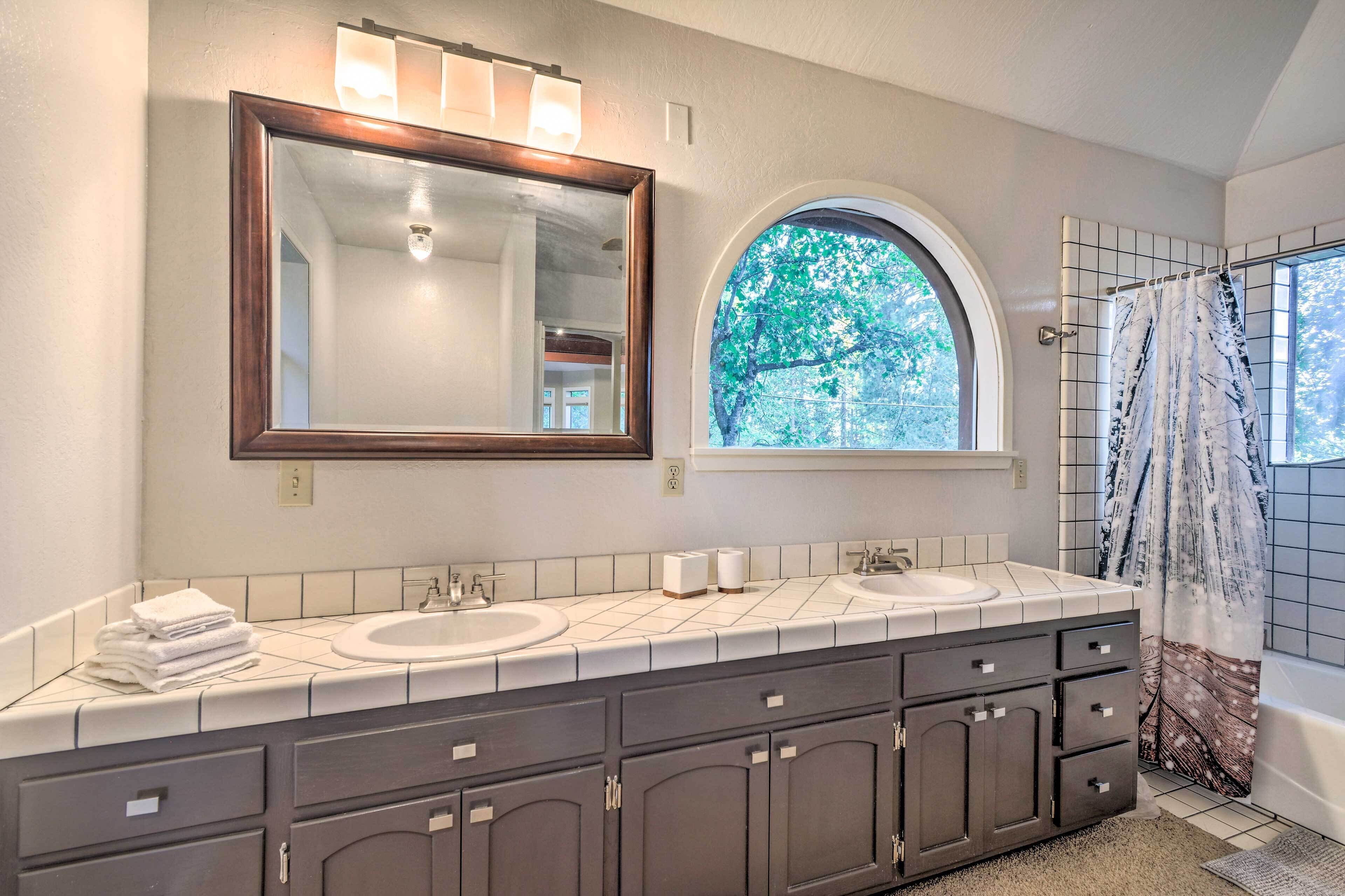 A bathroom with two sinks, a large mirror, and a window with a view of trees.