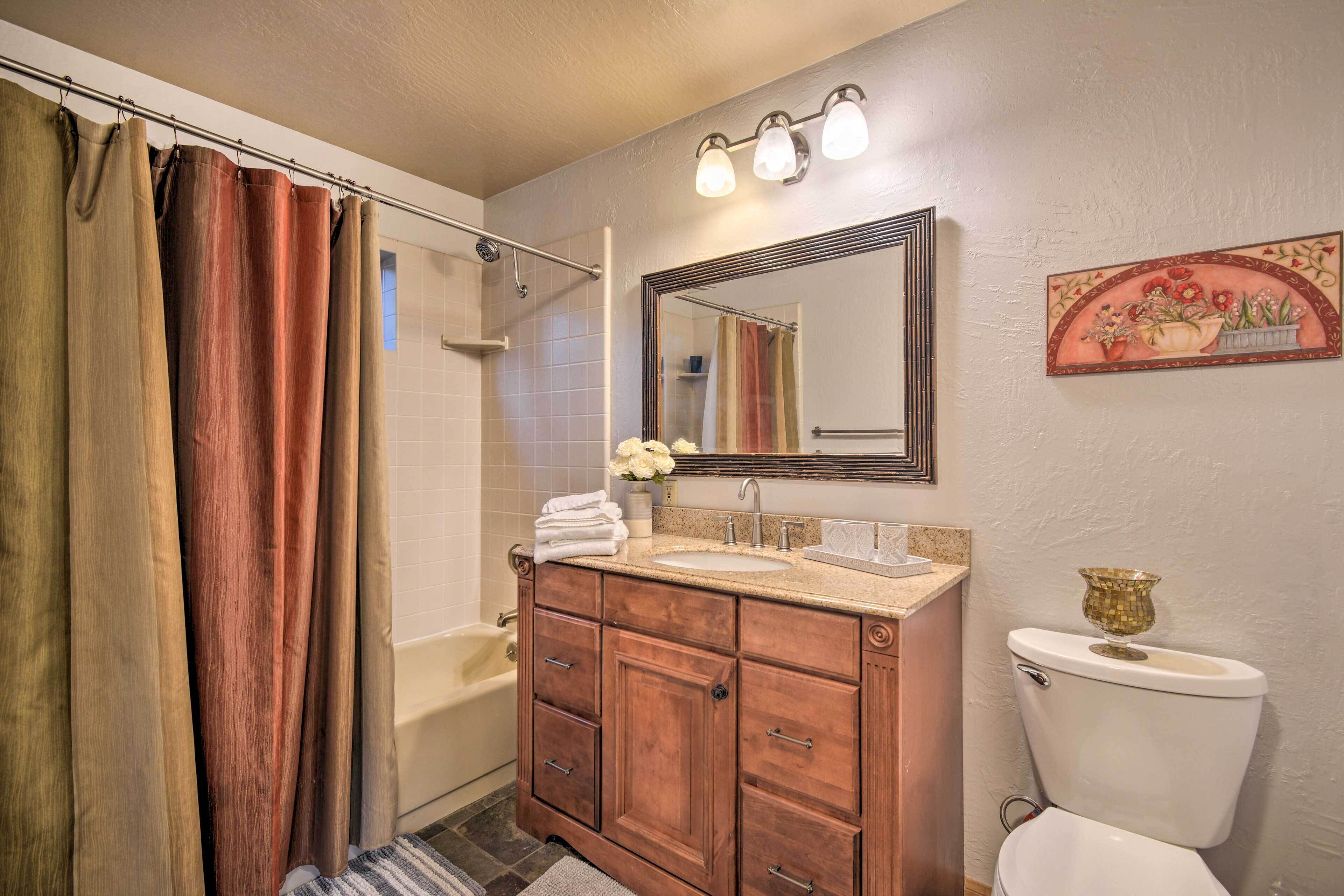 Une salle de bain avec un meuble-lavabo en bois, des toilettes blanches, un rideau de douche et un miroir avec éclairage intégré.
