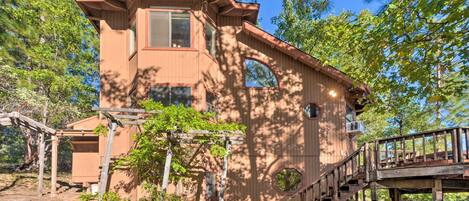 A wooden cabin with a staircase leading to a deck, surrounded by trees.