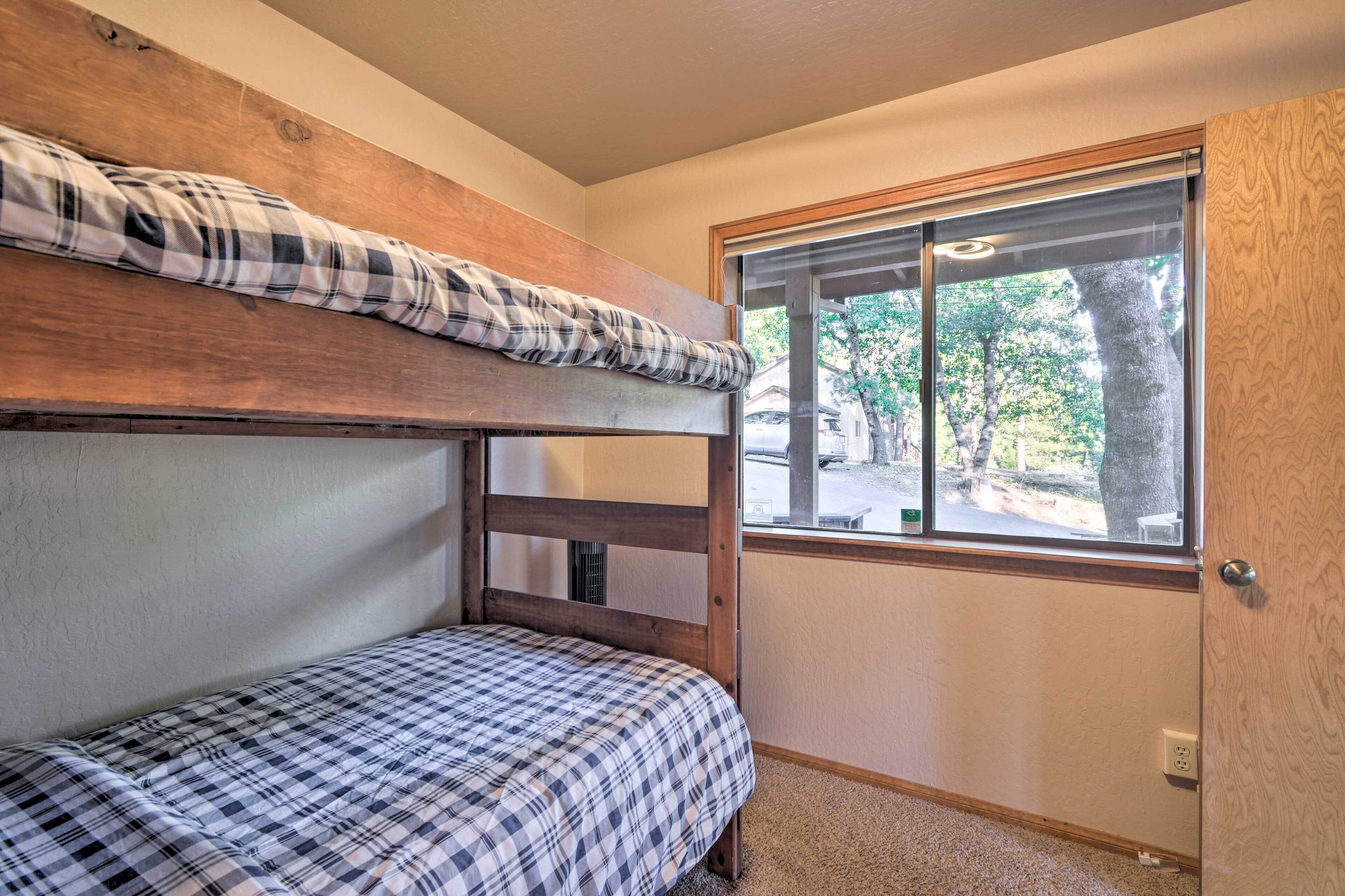 A bunk bed room with a window providing a view of trees and a bench outside.