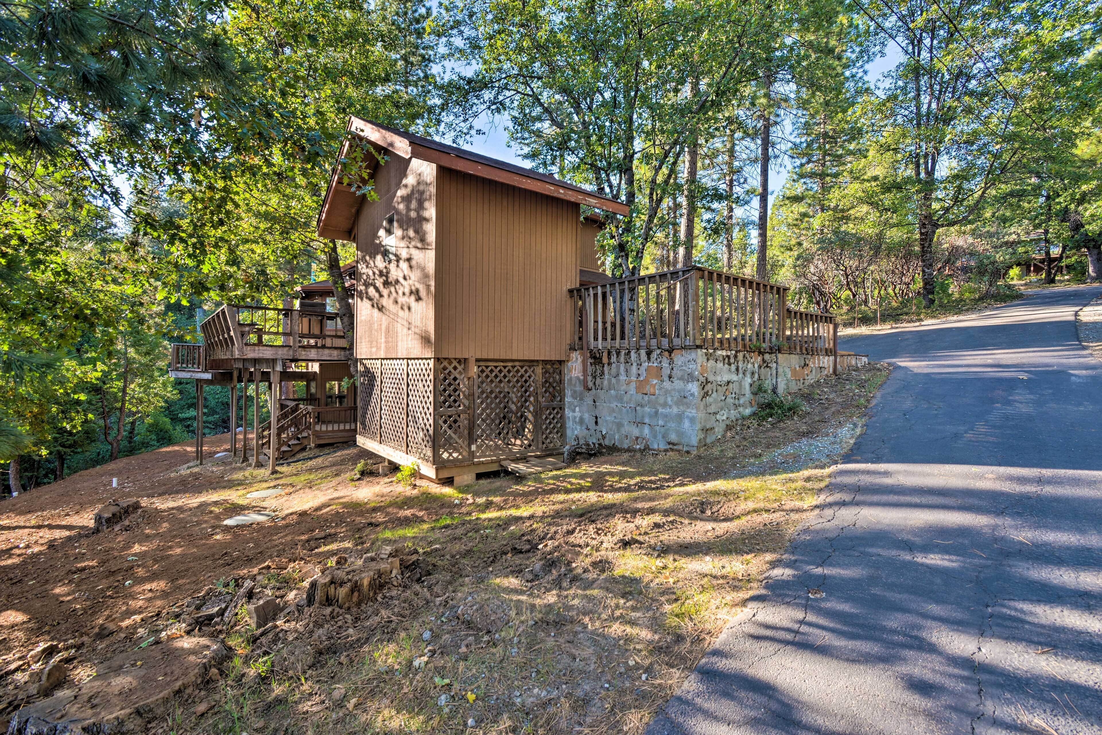 Un chalet rustique doté d’une terrasse en bois et d’un espace clôturé, le tout entouré d’arbres.