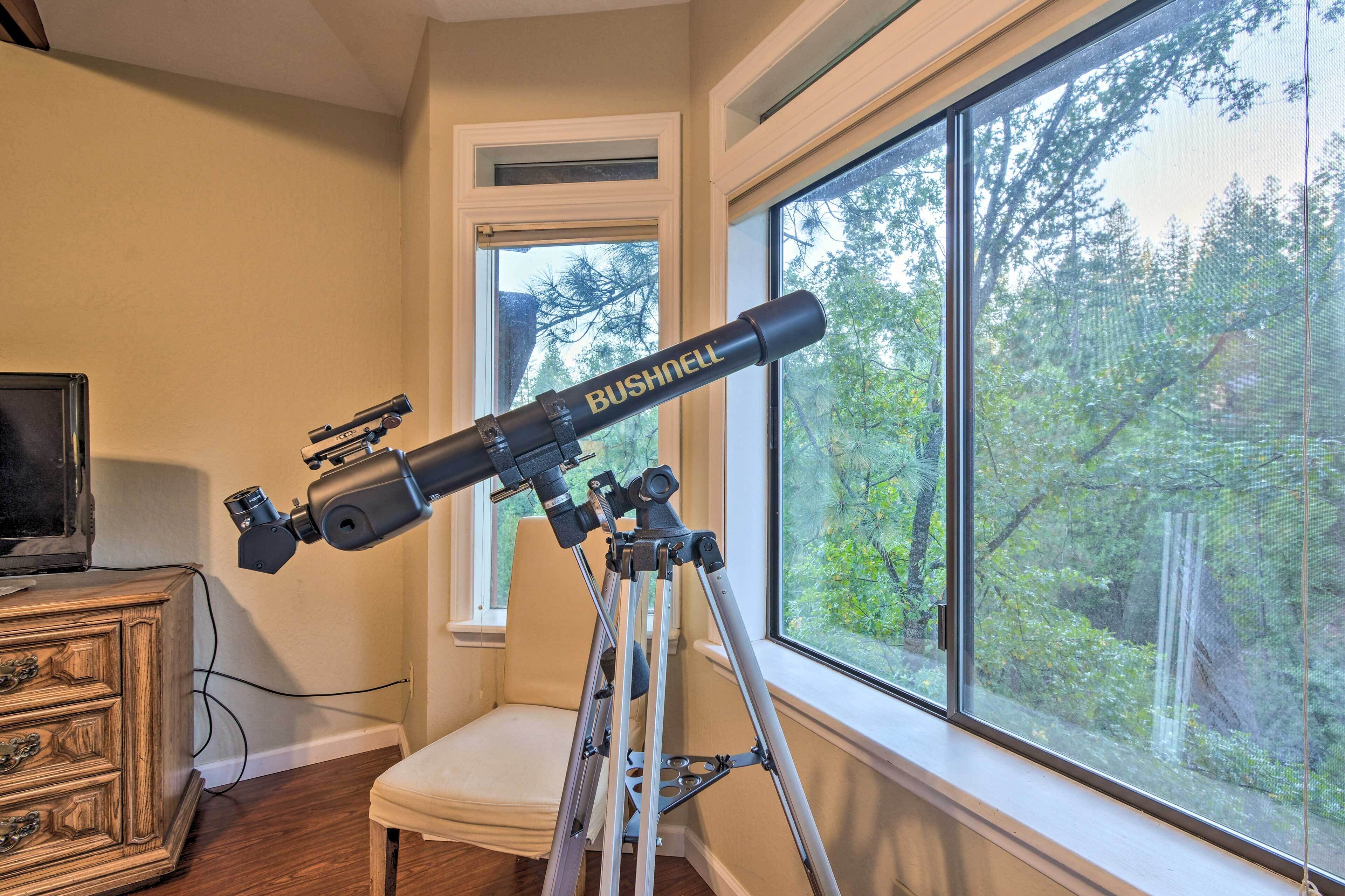 A telescope on a tripod in a room with a window overlooking a forest.
