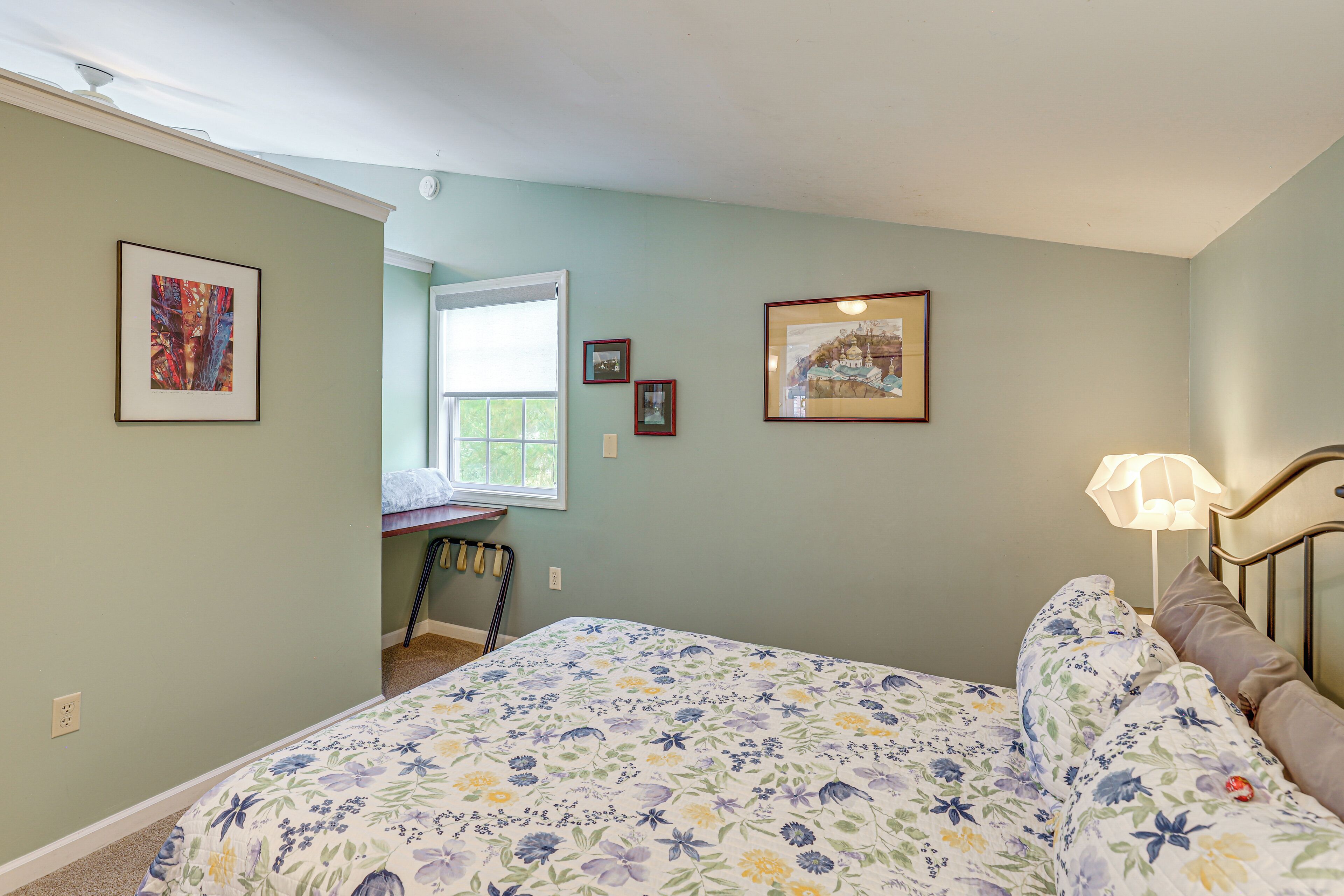 A bedroom with a floral bedspread, a desk, and a window with a view.