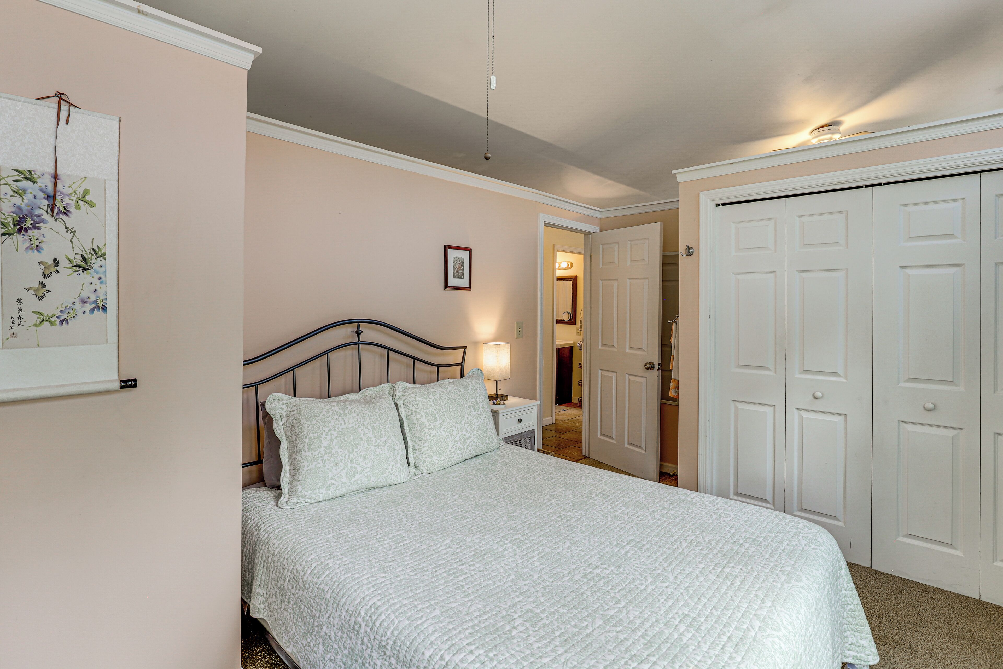 A bedroom with a bed, nightstand, and a door leading to another room.