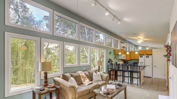 A spacious living room with a large window, a sofa, a coffee table, and a dining area with chairs and a table. - Blue Ridge Retreat w/ Deck: Hike, Sip & Explore! (Asheville)