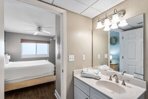 A hotel room with a bed, a bathroom with a sink and mirror, and a ceiling fan.