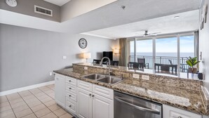 Una cocina moderna con encimeras de granito, electrodomésticos de acero inoxidable y un amplio ventanal con vistas a un balcón.