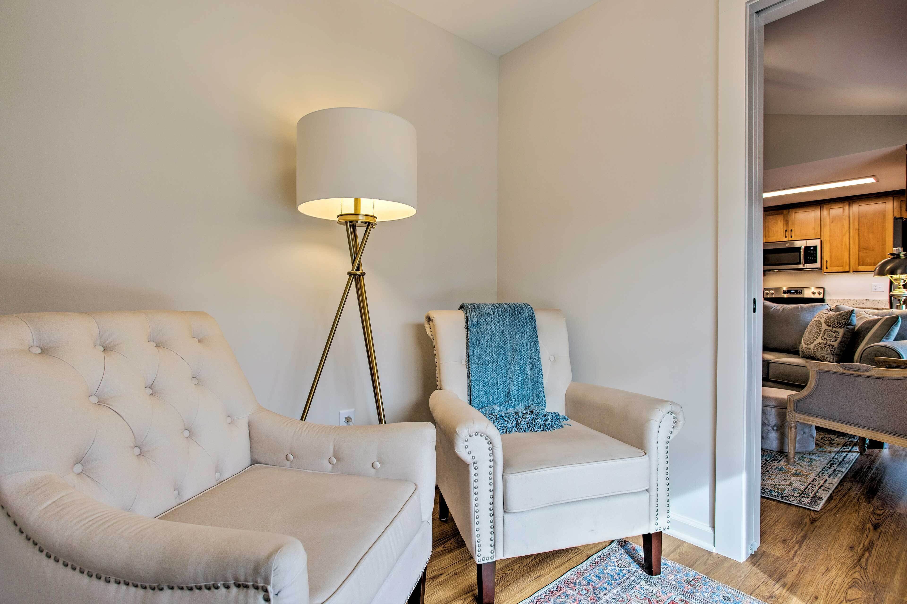 Un salon comprenant un fauteuil capitonné, un fauteuil plus petit avec un plaid bleu, et un lampadaire.