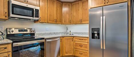 A kitchen with wooden cabinets, stainless steel appliances including a microwave, oven, dishwasher, and refrigerator.