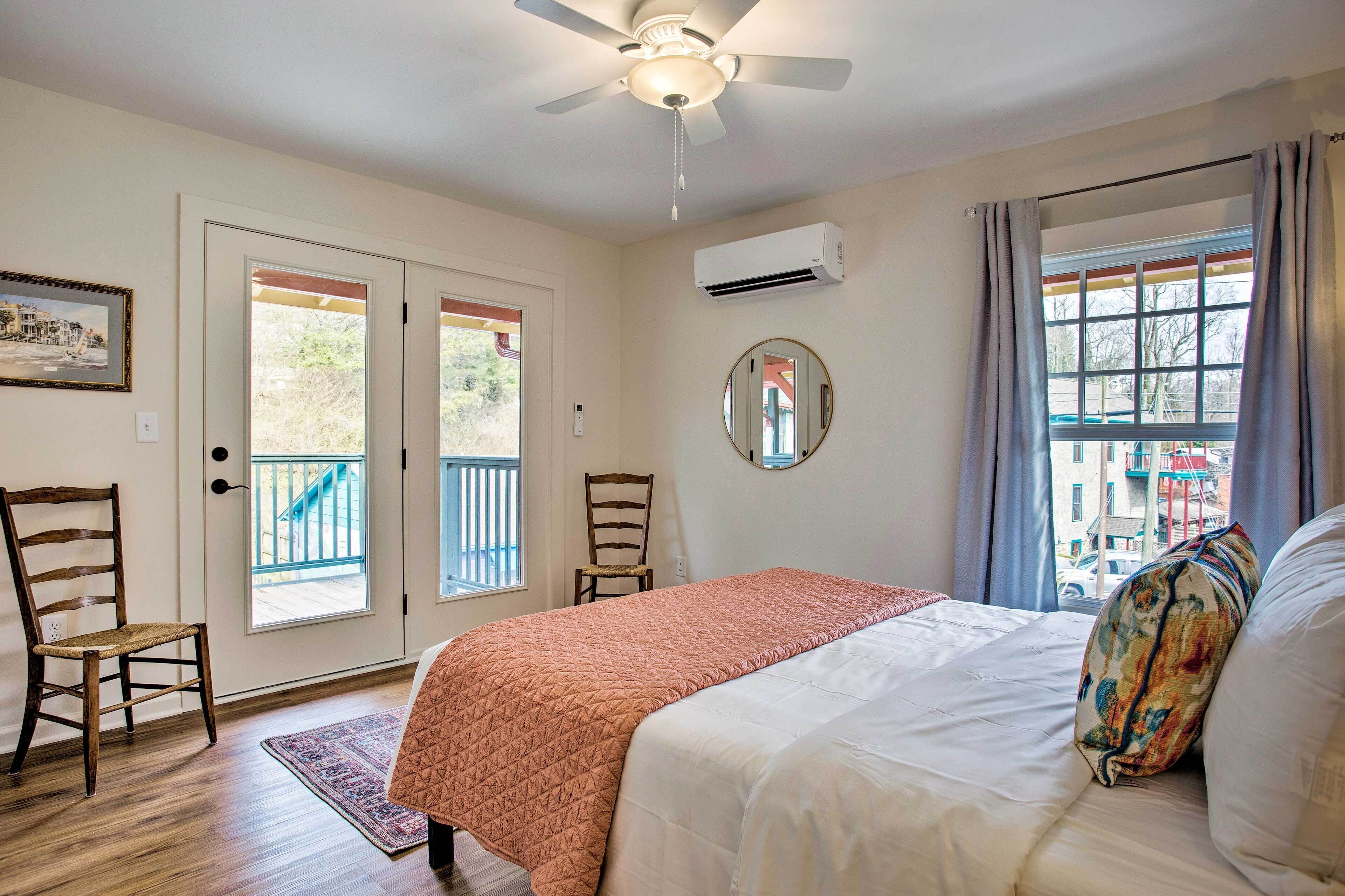 A bedroom with a bed, a ceiling fan, an air conditioning unit, a window with curtains, and a view of the outside.