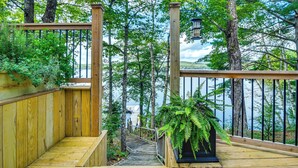 A wooden deck with a staircase leading to a viewing platform overlooking a lake, surrounded by trees. - Beautiful Embden Pond Cabin w/ Dock & Kayaks! (North Anson)