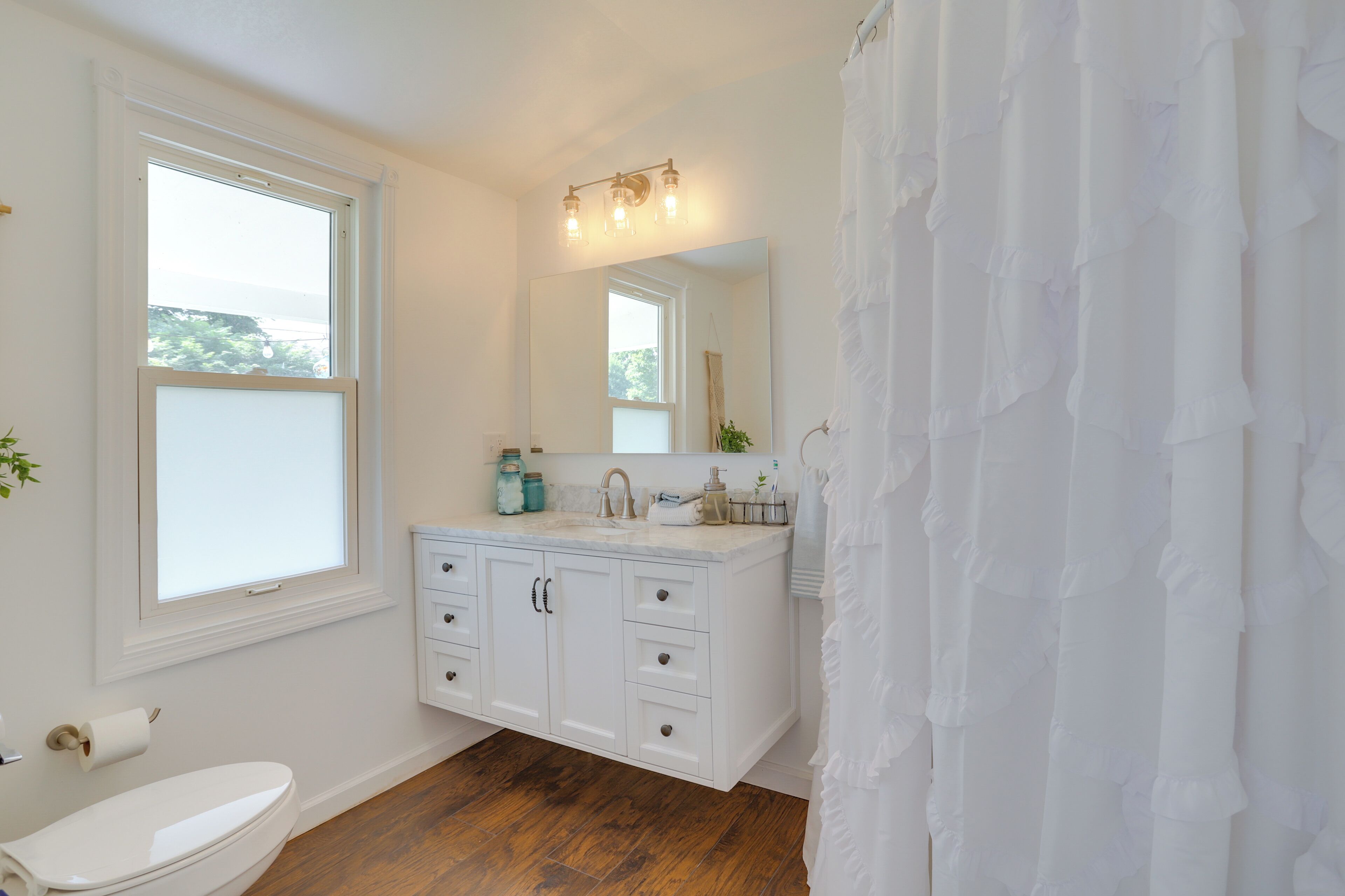 A bathroom with a toilet, a sink with a mirror, and a shower curtain.