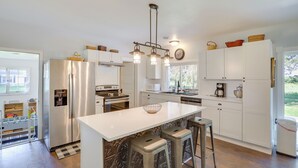 A modern kitchen with white cabinetry, stainless steel appliances, a central island with stools, and a hanging light fixture. - South Haven Farmhouse w/ Fire Pit, 4 Mi to Beach! (South Haven)