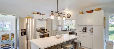 Una cocina moderna con armarios blancos, electrodomésticos de acero inoxidable, una isla central con taburetes y una lámpara colgante.