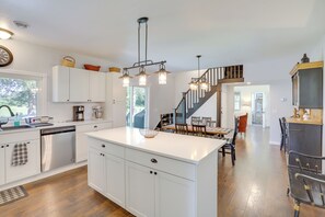 A spacious kitchen with white cabinetry, a central island, and a staircase leading to another level. - South Haven Farmhouse w/ Fire Pit, 4 Mi to Beach! (South Haven)