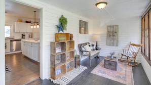 A spacious living area with a sofa, a rocking chair, and a coffee table. There is a kitchen visible in the background with white cabinets and a hanging light fixture. - South Haven Farmhouse w/ Fire Pit, 4 Mi to Beach! (South Haven)