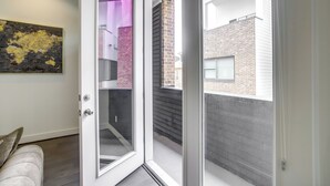 En skjutdörr i glas leder ut till en balkong med utsikt över en byggnad med tegelstensfasad och ett inre utrymme som är upplyst i lila.