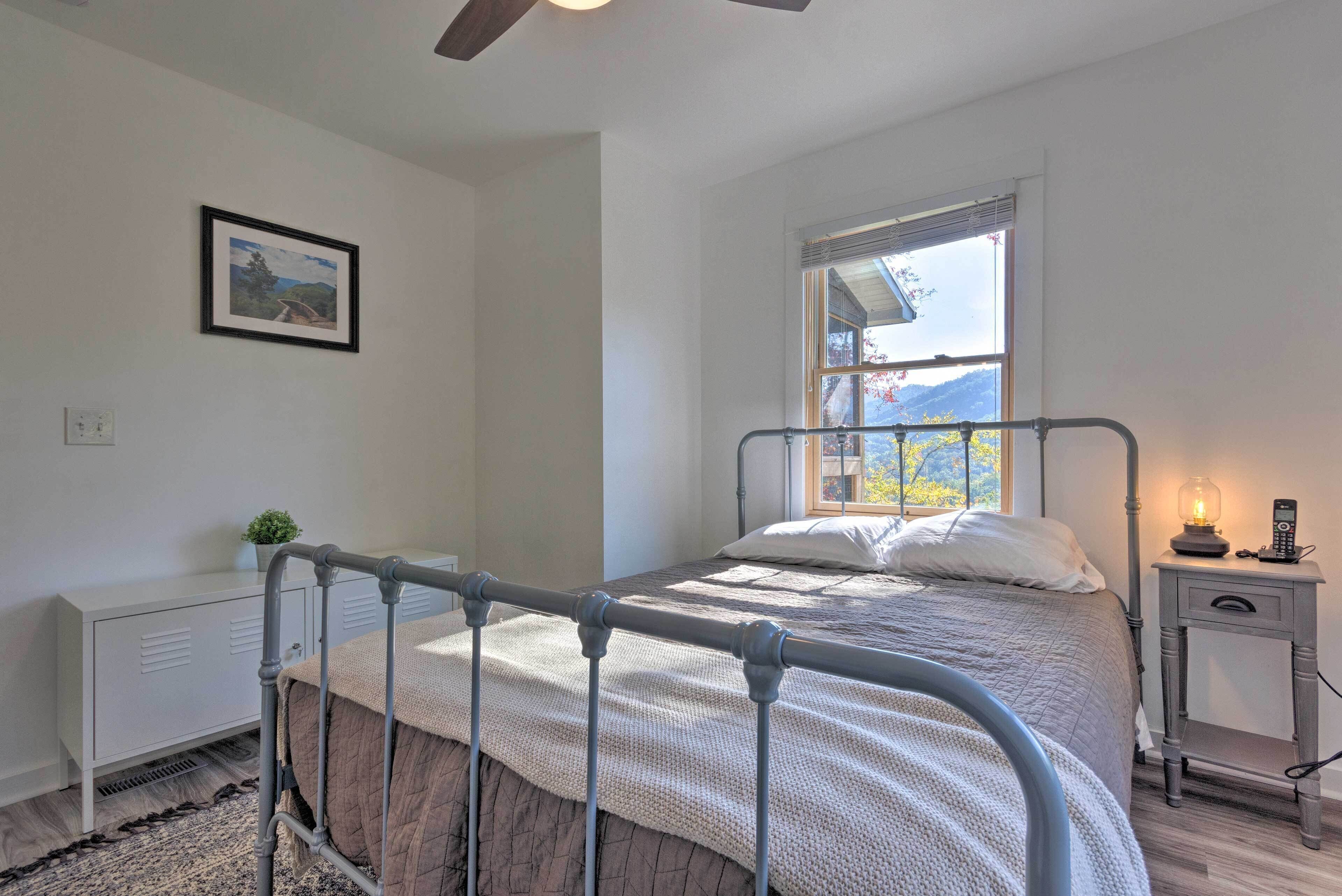 A bedroom with a metal bed frame, a bedside table with a lamp, a window with a view of mountains, and a radiator.