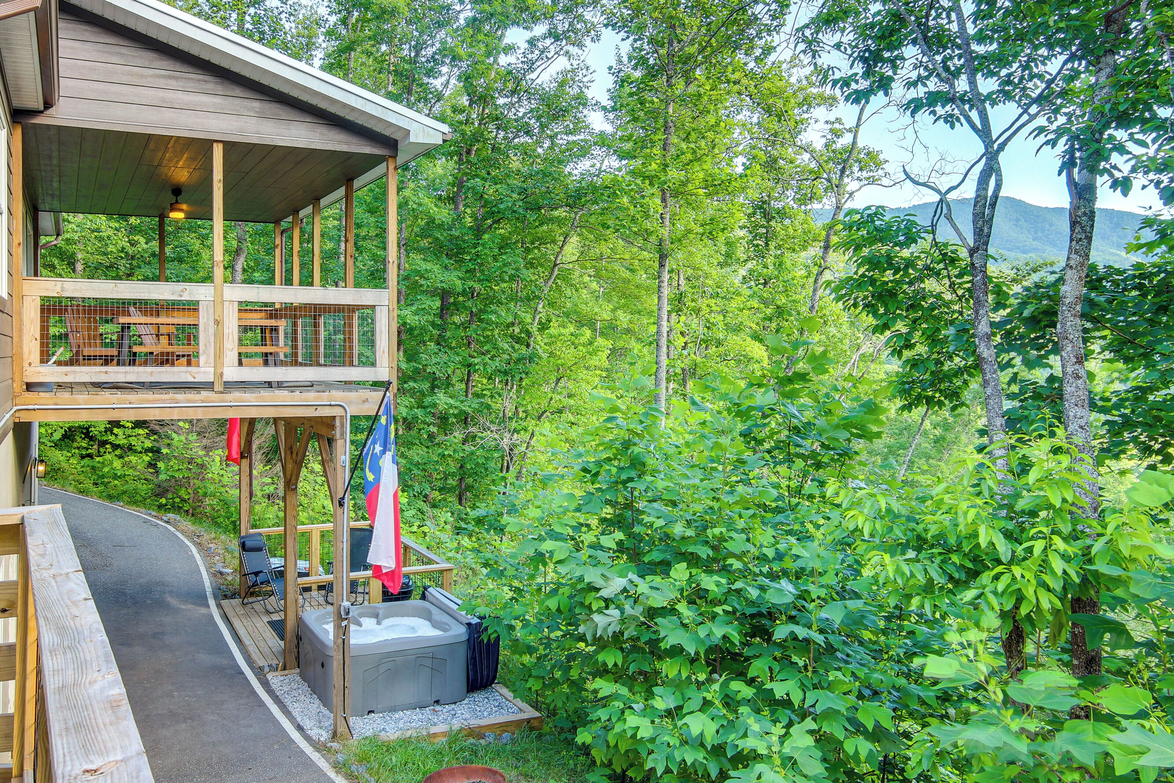 A wooden cabin with a deck, a hot tub, and a view of the surrounding forest.