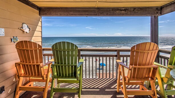 Eine überdachte Terrasse mit Adirondack-Stühlen, die auf einen Strand ausgerichtet ist.