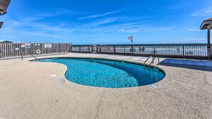 Ein Pool mit Holzterrasse und Metallgeländer, umgeben von Sand.