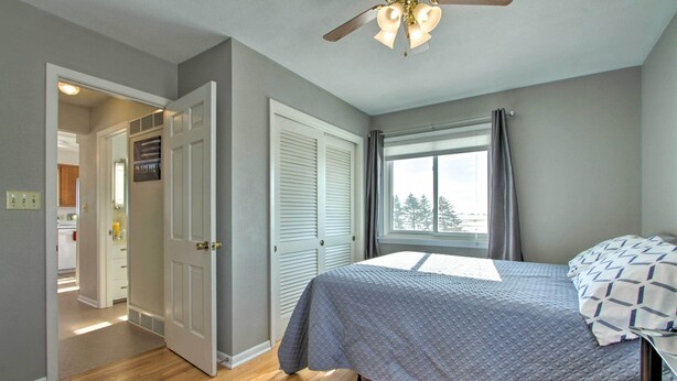 Ein Schlafzimmer mit einem Bett, einem Deckenventilator, einem Fenster mit Vorhängen und einer Tür zu einem anderen Raum.