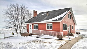 A red house with a white porch and a snow-covered yard. - Cozy Postville Retreat w/ Fireplaces & Yard! (Postville)