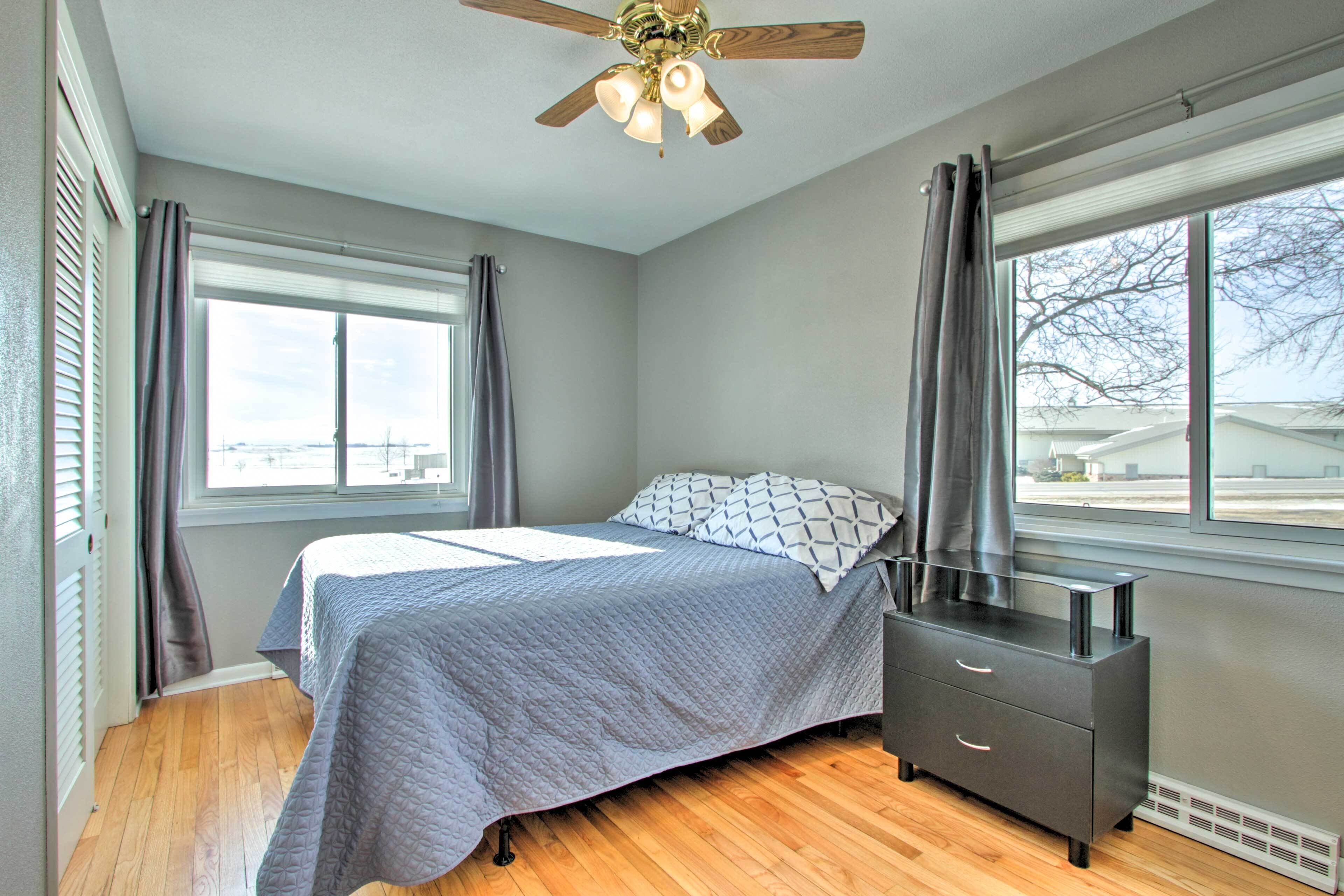 Un dormitorio con cama, cómoda, ventilador de techo y ventanas amplias.