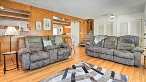 A spacious living room with two grey sofas, a wooden accent wall, a staircase, and a view of the kitchen. - Cozy Postville Retreat w/ Fireplaces & Yard! (Postville)