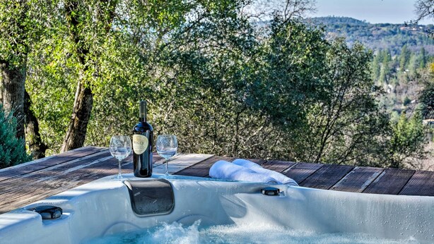 Un jacuzzi con una botella de vino y copas, rodeado de árboles y una vista panorámica.
