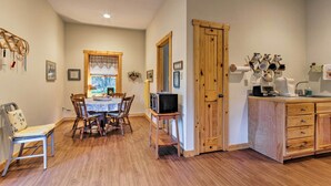 A cozy dining area with a wooden table and chairs, a television on a stand, and a kitchen area with wooden cabinets and a sink.