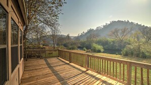Una terraza de madera con barandilla, con vistas a un área boscosa y una colina.