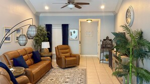 A living room with a brown leather sofa, a brown armchair, a patterned rug, a ceiling fan, and a wall clock. - Coastal Condo w/ Pool in South Padre Island! (South Padre Island)